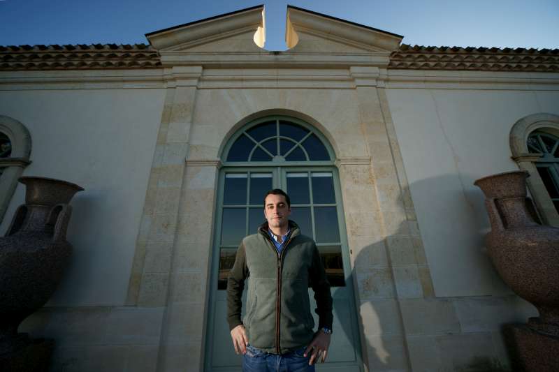 Olivier Berrouet stands with a gentle smile at the front door of Château Pétrus. The vines can be seen reflected in the glass of the door.